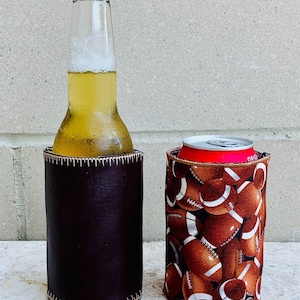 May include: Two insulated beverage holders, one brown leather and one with a football pattern. The holders are empty.