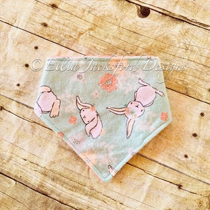 May include: A light blue and pink bandana with a floral pattern and pink bunnies. The bandana has a pink border and the text "Ellia Jackson Designs" is printed on the top.