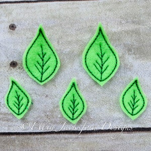 May include: Five green felt leaves with a simple vein design, sewn with green thread. The leaves are arranged in a staggered pattern on a light wood background.