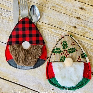 May include: Two Christmas gnome-themed utensil holders. The holder on the left is red and black plaid with a brown fuzzy beard. The holder on the right is burlap with a green holly design and a white fuzzy beard.