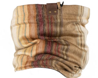 May include: A brown and beige striped neck gaiter with a leather patch that says "Lazy Traveler" and a metal buckle. The gaiter is made of a soft, warm fabric and can be worn as a neck warmer, face mask, or headband.