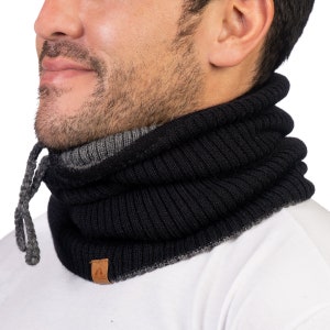 May include: A black and gray knit neck warmer with a ribbed design. The neck warmer has a drawstring and a small brown leather tag. The neck warmer is worn around the neck and covers the lower face.