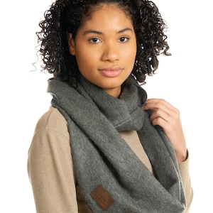 以下が含まれることがあります： 「ザ・ノース・フェイス」と書かれた茶色の革のパッチが付いた灰色のインフィニティスカーフです。