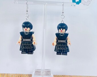 Może przedstawiać: Para kolczyków wiszących z czarnymi minifigurkami Lego ubranymi w czarne sukienki z białymi akcentami. Minifigurki mają czarne włosy i czerwone usta.