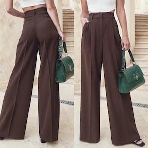 May include: Two views of brown wide-leg trousers with a high waist and belt loops. A green handbag with a gold-colored clasp and strap is held in each image. The trousers have pleats in the front.