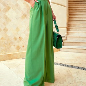 May include: Bright green wide-leg trousers with a high waist and pleats. The trousers are paired with a matching green handbag and black sandals. The outfit is completed with a white crop top.