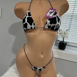 May include: A black and white cow print bikini top and matching string bottom. The bikini top has thin black straps and the bottom is a very small string style.