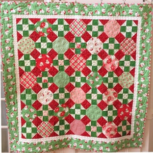 May include: A red, green and white quilt with a patchwork design. The quilt is made up of squares and circles, and features a variety of Christmas-themed patterns.