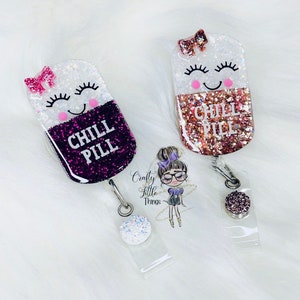 May include: Two glitter filled pill shaped resin keychains with a smiling face and the text "Chill Pill". The keychains are attached to clear retractable badge holders with glitter accents.