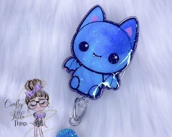 Puede incluir: Un portagafete retráctil transparente con un dije de murciélago azul con brillantina y un círculo azul con brillantina. El dije tiene una cara de dibujos animados linda con orejas rosadas y ojos blancos.