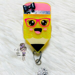 May include: A yellow glitter pencil with a pink eraser and a black bow. The pencil has a pink and black pair of glasses and a smiling face. The pencil is attached to a clear badge holder with a silver rhinestone charm.