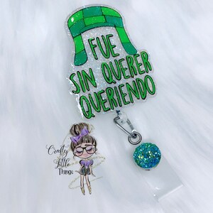 May include: Green and white glitter badge reel with a cartoon character and the text "FUE SIN QUERER QUERIENDO".