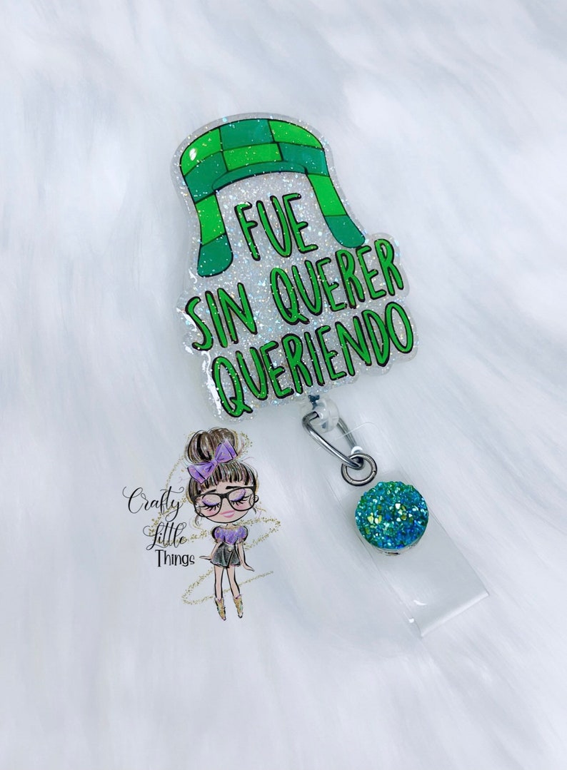 May include: Green and white glitter badge reel with a cartoon character and the text "FUE SIN QUERER QUERIENDO".