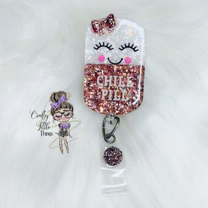 May include: A pink and white glitter resin badge holder with a smiling face and the text "CHILL PILL". The holder is attached to a clear plastic retractable badge reel with a pink glitter button.