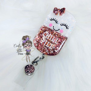 May include: A pink and white glitter resin badge holder with a smiling face and the words "Chill Pill" in white lettering. The badge holder is attached to a clear plastic badge holder with a silver clip.