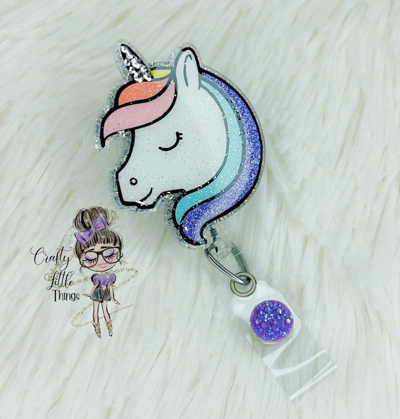 May include: A sparkly silver unicorn head with a rainbow mane and a purple tail, attached to a clear plastic badge holder with a purple glitter charm.