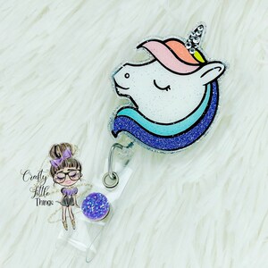 May include: A sparkly unicorn head badge reel with a blue, pink and white glitter design. The reel has a clear plastic backing and a purple glitter charm.