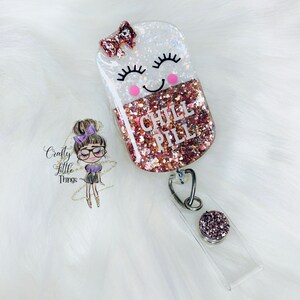 May include: A pink and white glitter resin badge holder with a smiling pill design. The pill has a pink bow and the text "CHILL PILL" in black lettering.
