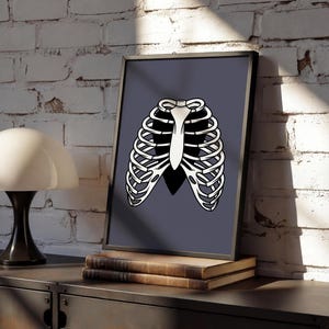 Art Print of a skeleton ribcage with a black heart encased onside on a blue/grey background shown in a modern home against a white brick wall sat framed on top of an industrial style sideboard.