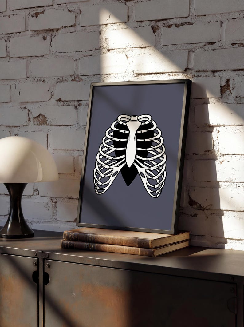 Art Print of a skeleton ribcage with a black heart encased onside on a blue/grey background shown in a modern home against a white brick wall sat framed on top of an industrial style sideboard.