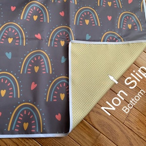 May include: A gray play mat with a rainbow and heart pattern. The mat has a white border and a non-slip bottom.