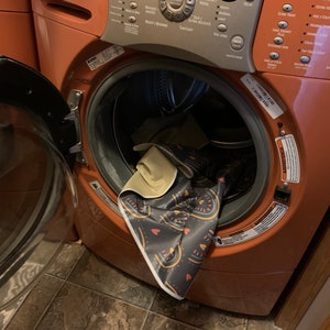 May include: A close-up of the inside of a red washing machine with a colorful patterned rug inside. The washing machine has a digital control panel with various buttons and settings.