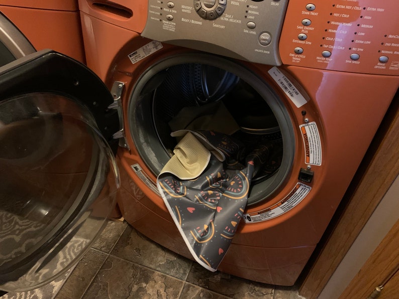 May include: A close-up of the inside of a red washing machine with a colorful patterned rug inside. The washing machine has a digital control panel with various buttons and settings.