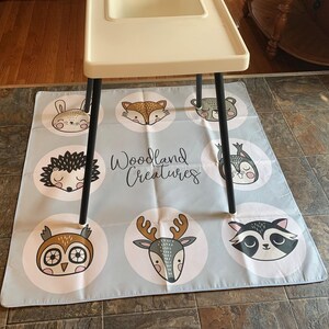 May include: A light blue play mat with a white border and a variety of woodland animal illustrations. The mat features a deer, owl, raccoon, hedgehog, bunny, and fox. The text "Woodland Creatures" is printed in white on the mat.
