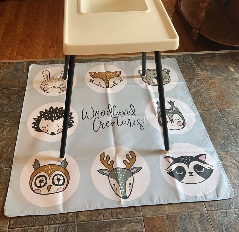 May include: A light blue play mat with a white border and a variety of woodland animal illustrations. The mat features a deer, owl, raccoon, hedgehog, bunny, and fox. The text "Woodland Creatures" is printed in white on the mat.