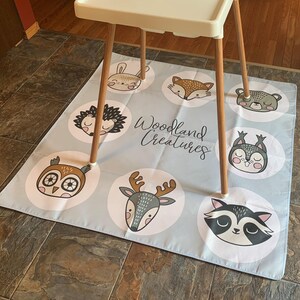 May include: A blue and white play mat with a woodland creatures theme. The mat features illustrations of a fox, owl, deer, raccoon, hedgehog, bunny, squirrel, and bear. The text "Woodland Creatures" is printed in black on the mat.