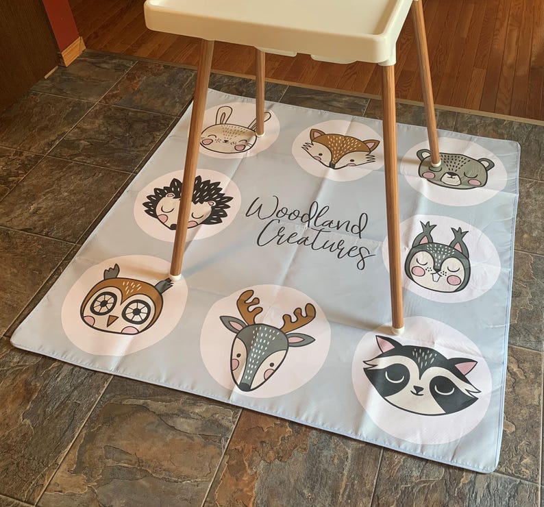 May include: A blue and white play mat with a woodland creatures theme. The mat features illustrations of a fox, owl, deer, raccoon, hedgehog, bunny, squirrel, and bear. The text "Woodland Creatures" is printed in black on the mat.