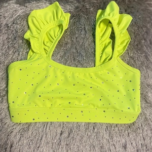 May include: Neon yellow crop top with ruffled straps and scattered rhinestone embellishments. The top has a scoop neckline and a fitted silhouette. The fabric appears to be a smooth, stretchy material. The overall style is playful and eye-catching.