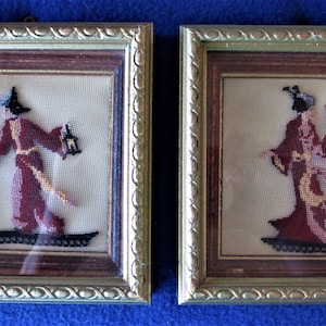 May include: Two framed needlepoint embroidery pieces. The left piece features a figure in a red robe and hat holding a lantern. The right piece features a figure in a red and gold robe holding a fan.