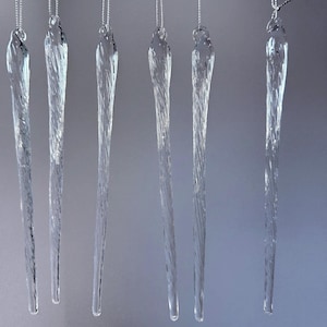 May include: Six clear, twisted glass icicle ornaments hanging vertically from thin silver strings. Each icicle features a tapered, elongated shape with a spiraling texture throughout the body, mimicking the appearance of natural frozen water.