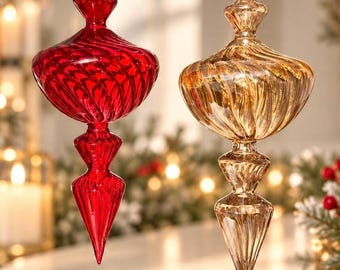 May include: Two finial-shaped glass ornaments hanging from gold strings. One ornament is a deep, translucent red, and the other is a translucent gold. Both feature a spiralling, ribbed texture that tapers to a pointed bottom and a decorative top.