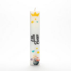 Puede incluir: Vela blanca con una corona amarilla, corazones azules y estrellas amarillas. La vela tiene el texto "little prince" impreso en ella. La vela también presenta una pequeña ilustración de un príncipe con un zorro.