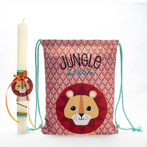 Puede incluir: Una bolsa de cordón roja con un patrón geométrico blanco y rojo. La bolsa tiene una cara de león con una melena amarilla y las palabras "Jungle Dream" impresas en ella. También se muestra una vela blanca con una cinta amarilla y una pequeña decoración de cara de león.