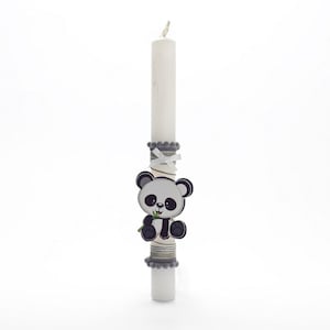 Puede incluir: Una vela blanca con una cinta gris y blanca y una decoración de oso panda. El oso panda está sosteniendo un brote de bambú verde.