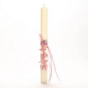 Puede incluir: Una vela blanca con decoraciones de bailarina rosa y acentos de cinta blanca y rosa.