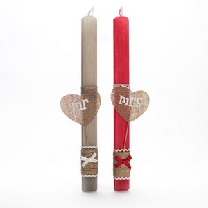 Puede incluir: Dos velas de boda, una gris y otra roja, con corazones de arpillera que dicen "Mr." y "Mrs." adjuntos.
