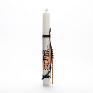 Puede incluir: Vela blanca con una cinta negra y marrón y una mano sosteniendo un mando de videojuego. La mano está pintada en la vela.