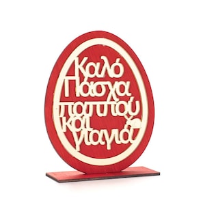 Puede incluir: Adorno de madera rojo en forma de huevo con una inscripción dorada que dice "Kaló Pascha,  pastitsiou kai Yiamá!"