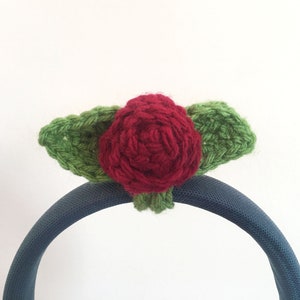 May include: A red crocheted rose with green crocheted leaves attached to a blue headband.