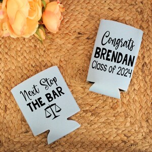 May include: Two blue and white can coolers with black text. One cooler says "Congrats Brendan Class of 2024". The other cooler says "Next Stop The Bar" with a scale of justice symbol.