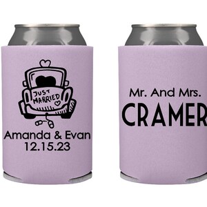 May include: Two lavender can coolers with black text. One cooler has a cartoon car with the text "Just Married" and the names "Amanda & Evan" and the date "12.15.23". The other cooler has the text "Mr. And Mrs. CRAMER".