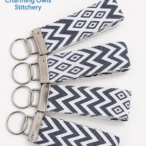 May include: Four fabric keychains featuring a dark gray and white geometric chevron and diamond pattern. Each keychain has a silver-toned metal clamp and a circular split ring. The logo for Charming Owls Stitchery is visible in the top left corner.