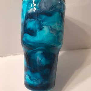 Puede incluir: Un vaso azul y blanco marmoleado con tapa negra. El vaso tiene un patr&oacute;n de remolino de azul, blanco y negro.