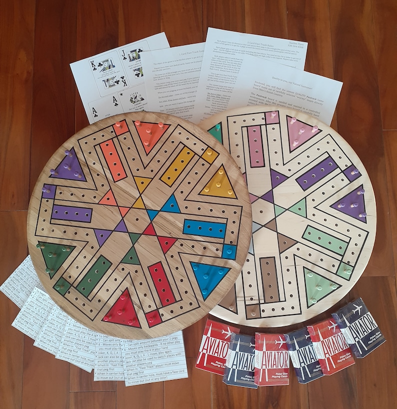 May include: Two wooden board games with colorful geometric designs and peg holes. The boards are round with triangular and rectangular sections in various colors. Several decks of "Aviator" playing cards and instruction sheets are also visible.
