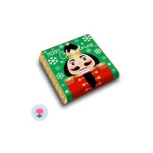 May include: A rectangular Christmas gift box with a green background and a nutcracker design. The box features the words "Merry Christmas" and snowflakes. The nutcracker has a black mustache and beard, and wears a red uniform.