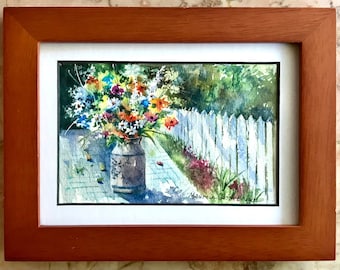 May include: A watercolor painting of a bouquet of colorful flowers in a vase, set against a white picket fence and a green garden background. The painting is signed "Maureen Gaskin Brown".
